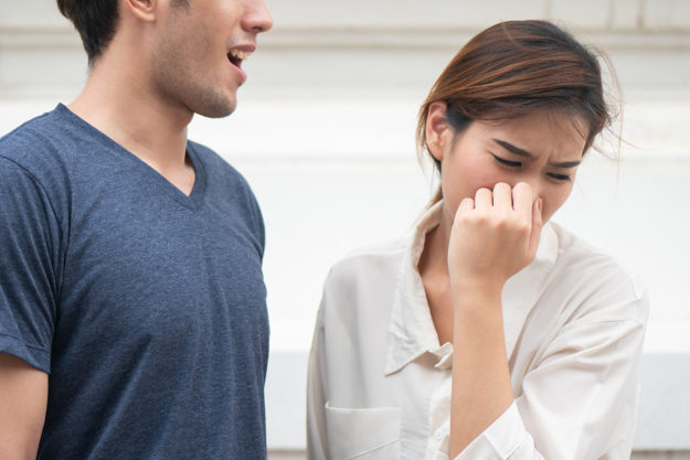 causes of bad breath Man breathing close to a woman who is trying not to smell his breath